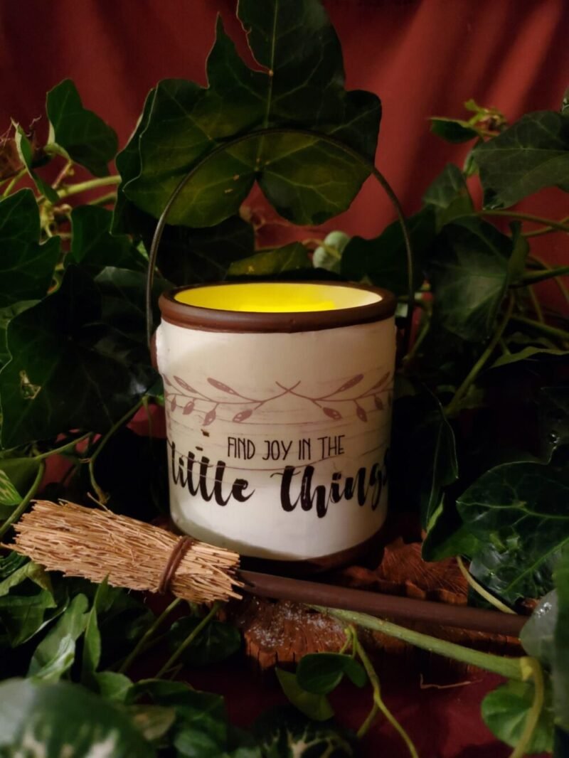 A candle holder with text - Find Joy In The Little Things. It's surrounded by ivy and a tiny witches broom.