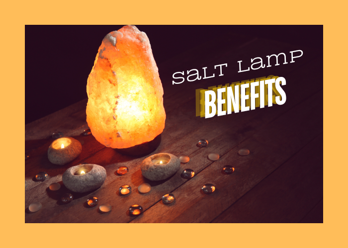 A salt lamp with candles and clear crystals around it on a wood table.